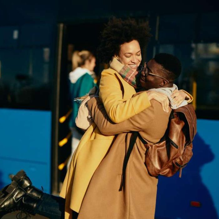 happy-black-couple-having-fun-embracing-while-meeting-bus-station