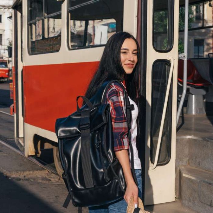 smiling-woman-carrying-backpack-standing-near-tram-street